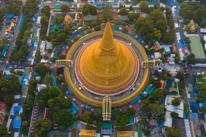Aerial top view of Phra Pathommachedi temple at sunset. The golden buddhist pagoda with residential houses, urban city of Nakorn