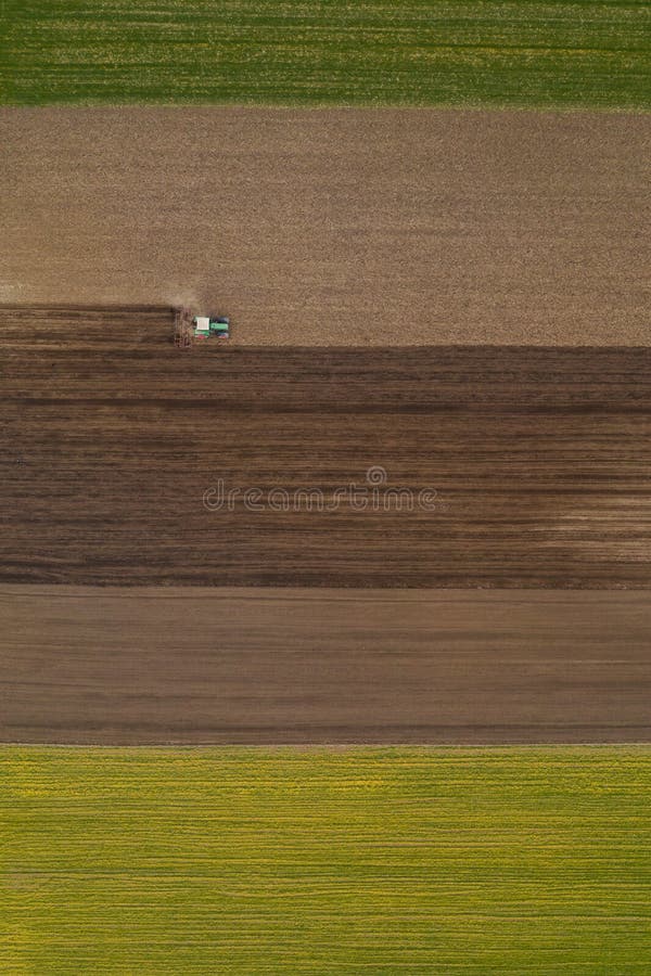 Aerial view of agricultural tractor tilling and harrowing ploughed field, directly above drone pov