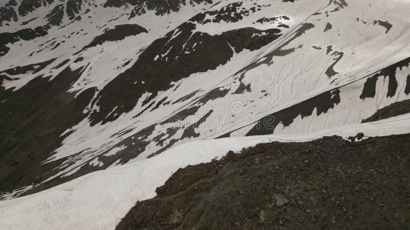 Aerial view of alpinist hiking with backpack in high snow-covered mountains. Man trekking on rocky and snowy terrain stock video footage
