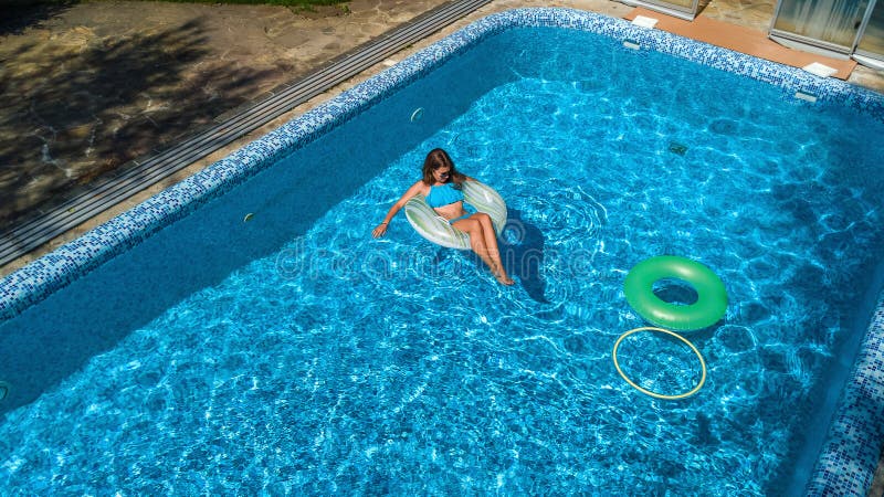 Aerial view of beautiful girl in swimming pool from above, swim on inflatable ring donut and has fun in water on family vacation