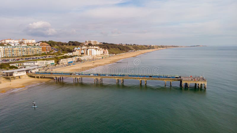 An aerial view of the Boscombe Beach with sandy beach, calm flat water and pier under a cloudy sky with some blue sky