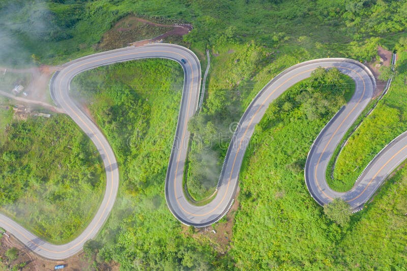 Aerial view of cars driving on curved, zigzag curve road or street on mountain hill with green natural forest trees in rural area