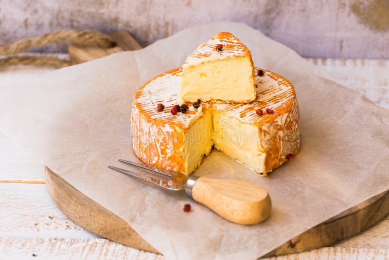 Aerial view of cut slice of French or German soft cheese with orange rind with mold, creamy texture, red pepper corns, waxed paper stock photo