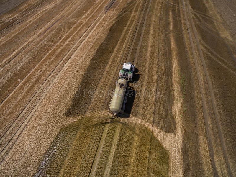 Aerial view of a farming tractor with a trailer fertilizes a freshly plowed agriculural field with manure in germany