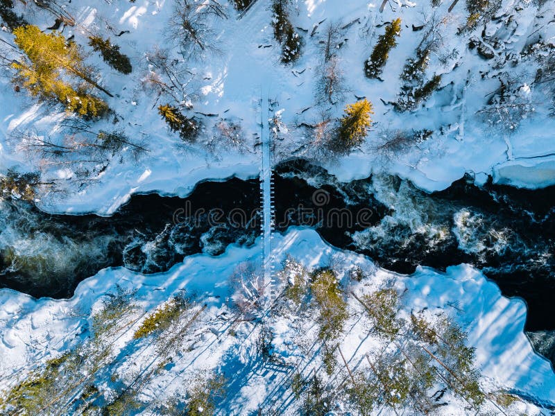 Aerial view of fast river with suspension foot bridge. Snow winter forest in Finland