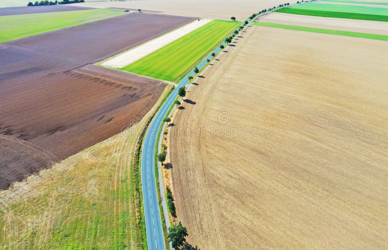 Aerial view of a grey asphalted narrow country road, which runs arcuately through a landscape with fields and meadows