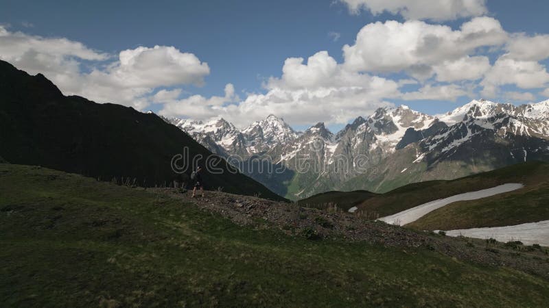 Aerial view of Koruldi mountain lakes and Svaneti peaks. Man hiker walks by. Snow patches and green meadows. Scenic stock video