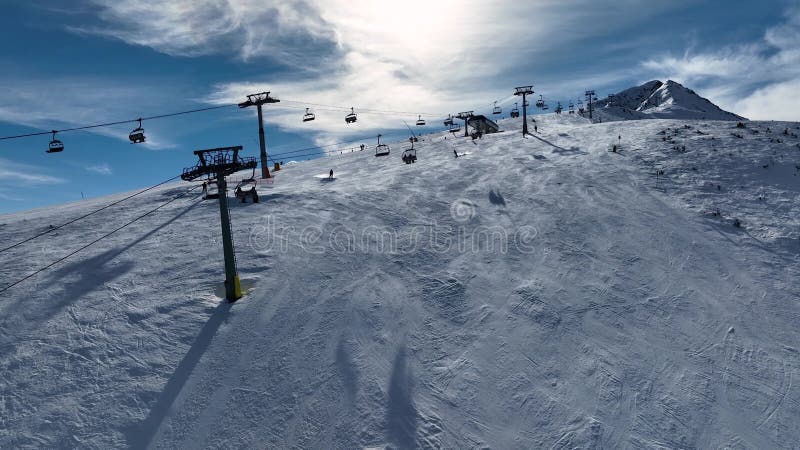 Aerial view over snowy mountain winter forest with chair lift at ski resort. Ski lift cable car stock footage