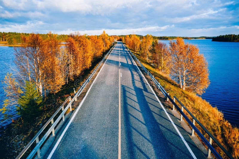Aerial view of road and forest in autumn colors with blue water lake