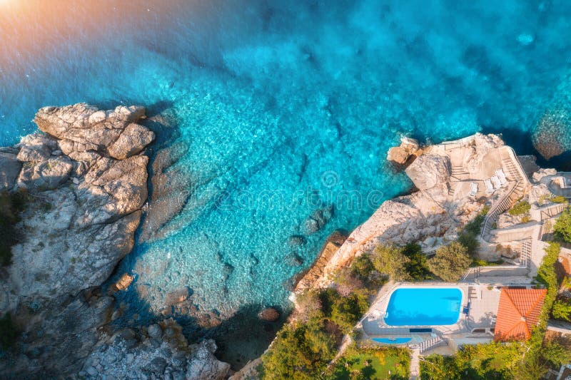 Aerial view of rocky beach, pool, green trees and blue sea