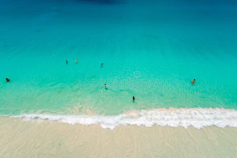 Aerial view of sandy beach with tourists swimming in beautiful clear sea water.