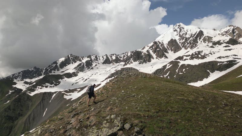 Aerial view of solo alpinist man with backpack climbing high mountains. Adventurer ascends rocky terrain under cloudy stock footage