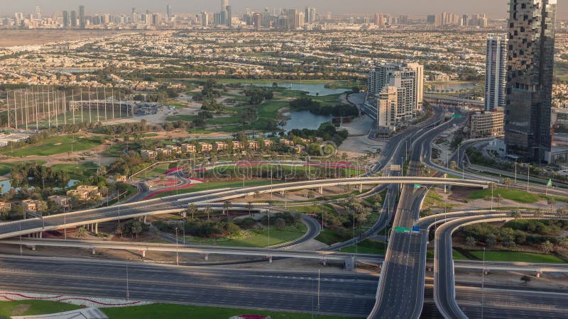 Aerial view to Golf course green lawn with lakes and big highway junction, villa houses behind it timelapse. Village triangle and circle district. Top view from Dubai marina skyscraper. Aerial view to Golf course green lawn with lakes and big highway junction, villa houses behind it timelapse. Village triangle and circle district. Top view from Dubai marina skyscraper.