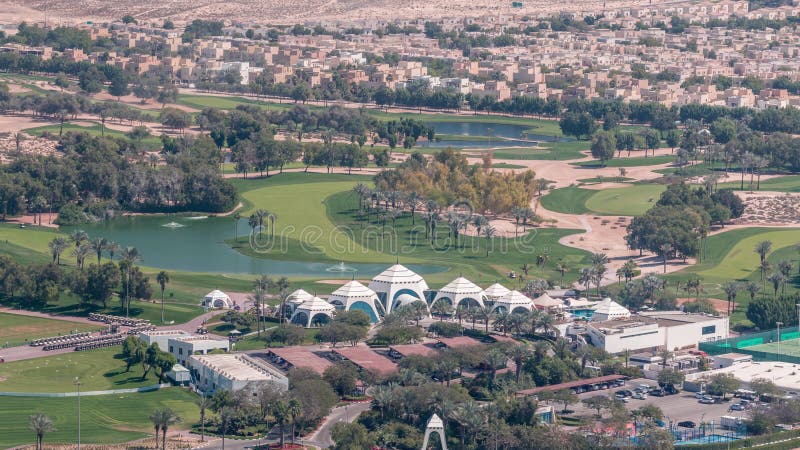 Aerial view to Golf course green lawn and lakes, villa houses behind it timelapse. Palms around parking lot. Top view from Dubai marina skyscraper. Aerial view to Golf course green lawn and lakes, villa houses behind it timelapse. Palms around parking lot. Top view from Dubai marina skyscraper.