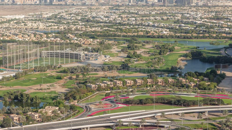 Aerial view to Golf course green lawn and lakes, villa houses behind it timelapse. Village triangle and circle district. Top view from Dubai marina skyscraper with traffic on overpass. Aerial view to Golf course green lawn and lakes, villa houses behind it timelapse. Village triangle and circle district. Top view from Dubai marina skyscraper with traffic on overpass