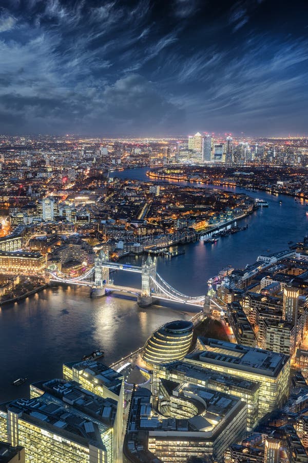 Aerial view to the illuminated Tower Bridge and financial district Canary Wharf in London during night, United Kingdom. Aerial view to the illuminated Tower Bridge and financial district Canary Wharf in London during night, United Kingdom