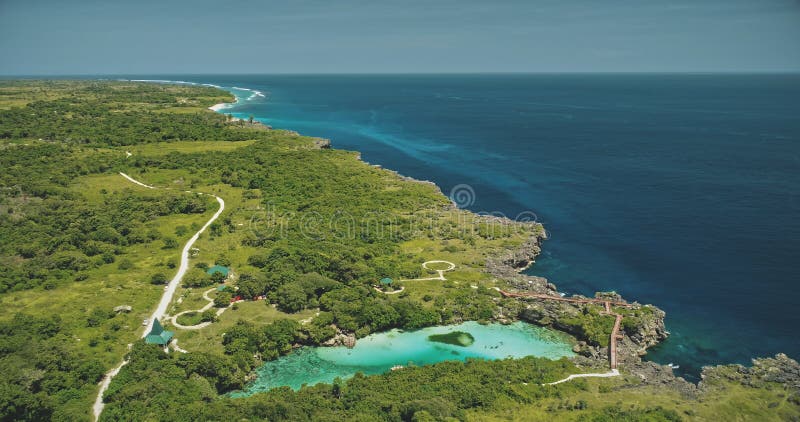 Aerial view of turquoise salt water lake at green tropic trees. Buildings, road at greenery valley