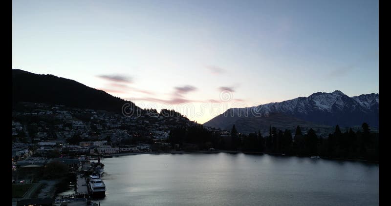 Aerial view of Wakatipu lakeshore with buildings at sunrise, with snowy mountain in the background stock video footage