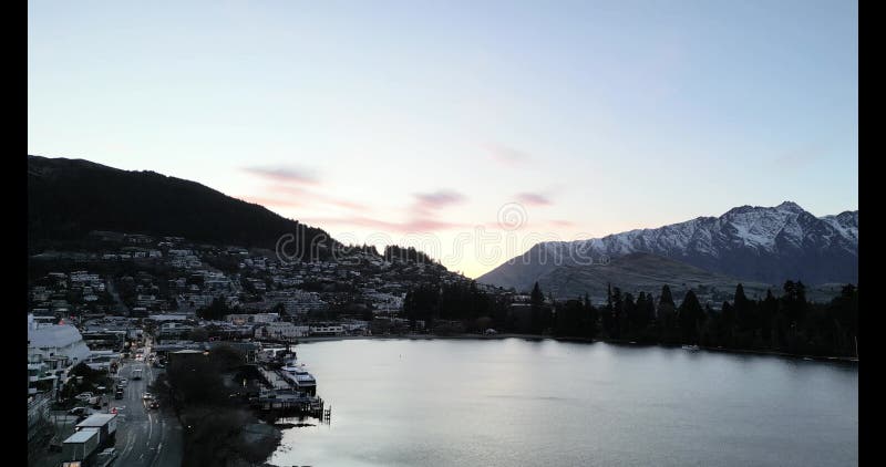 Aerial view of Wakatipu lakeshore with buildings at sunrise, with snowy mountain in the background stock video