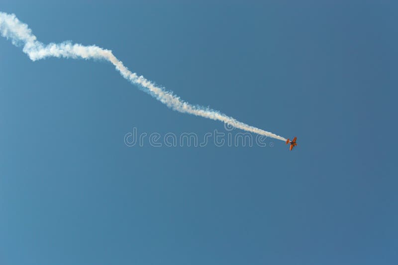 Aerobatic plane leaving a white smoke trail in the blue sky.