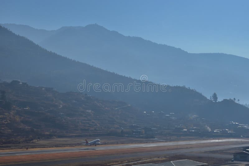 Aeroporto nas montanhas - But?o de Paro Paisagem da montanha com vila e o mini aeroporto na pista de decolagem um plano tenta dec imagem de stock Aeroporto nas montanhas - But?o de Paro Paisagem da montanha com vila e o mini aeroporto na pista de decolagem um plano tenta dec imagem de stock
