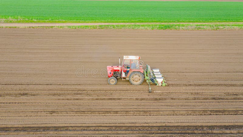 Above sidelong view, of tractor as pulling mechanical seeder machine over arable field, soil, planting new cereal crop, corn, maize. Above sidelong view, of tractor as pulling mechanical seeder machine over arable field, soil, planting new cereal crop, corn, maize