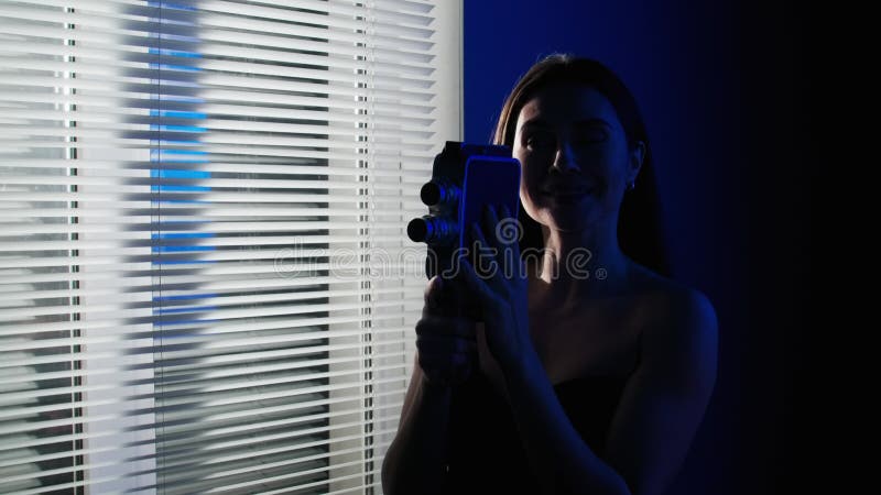 Afbeelding van een aantrekkelijk vrouwelijk model in studio. brunette vrouw in blauw - neonlicht , vlak bij raam , jalousie