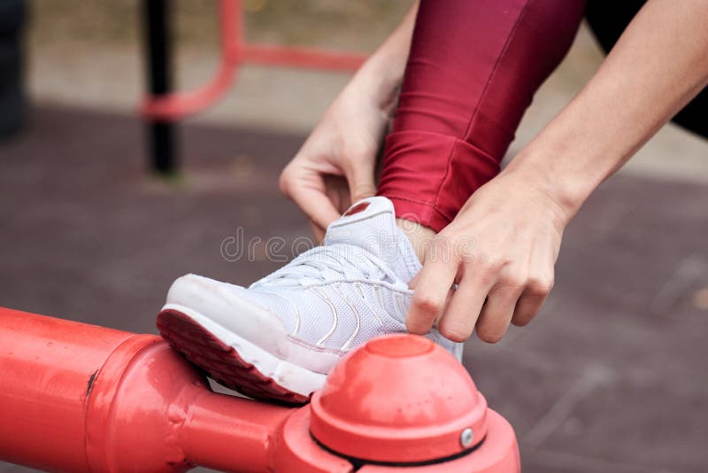 Close-up picture of hands, tying laces on white sport shoes. Woman, wearing red magenta leggings, putting on white sneakers for fitness training. Close-up picture of hands, tying laces on white sport shoes. Woman, wearing red magenta leggings, putting on white sneakers for fitness training