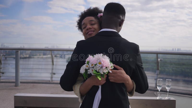 Afectuosa joven y delgada novia afroamericana abrazando a novio al aire libre sonriendo. retrato de una mujer amorosa abrazándose