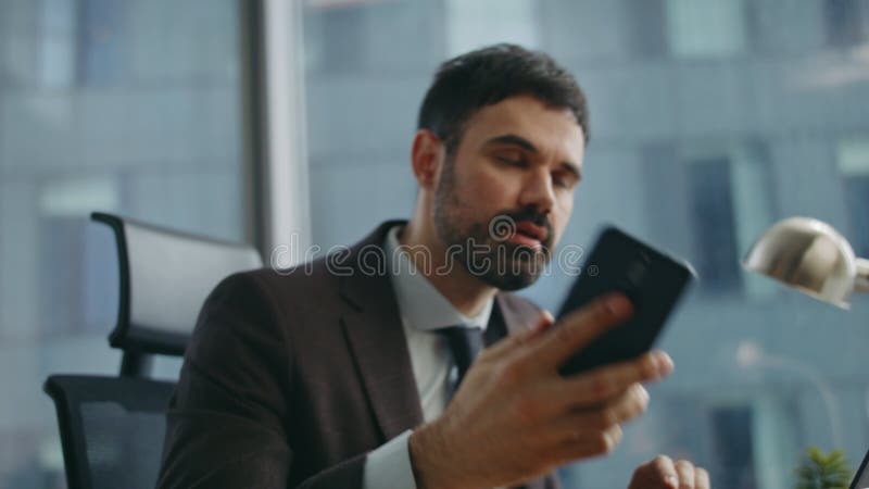 Affarato uomo d'affari che guarda il cellulare seduto alla scrivania da vicino