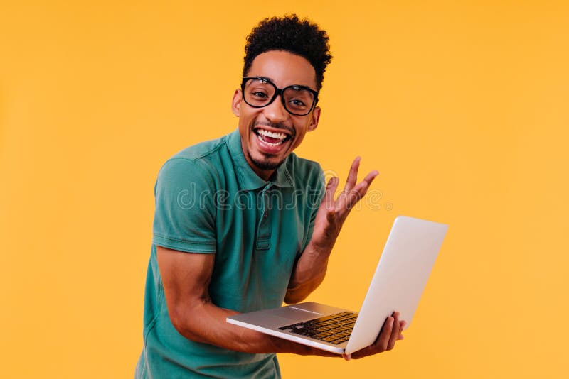 Affascinante freelance maschile con occhiali sorridenti di sfondo giallo. studente africano estatico immagine stock