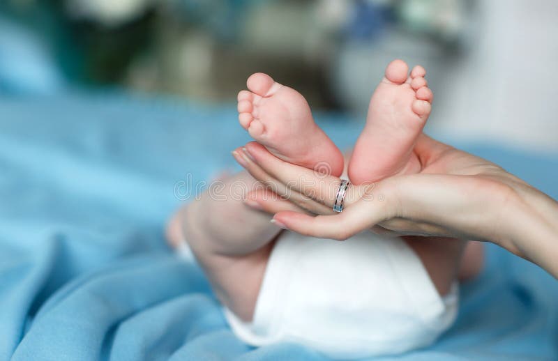 Affectionate mother`s hands gently support legs baby