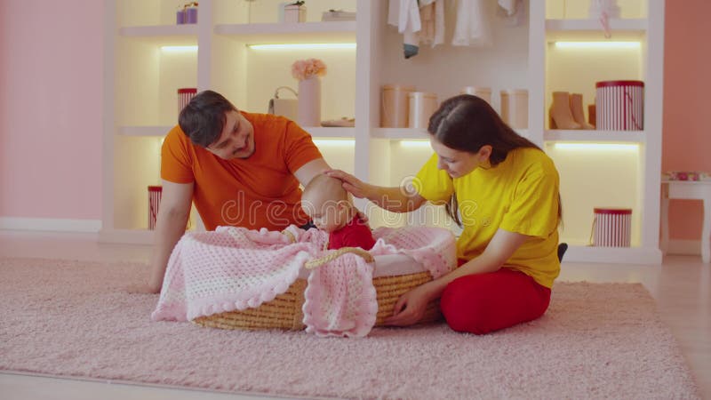 Affectionate parents bonding and caressing cute infant baby in cradle basket