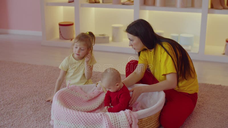 Loving mother teaching little daughter to take care and play with infant baby