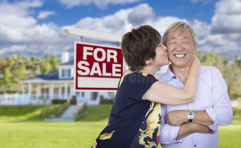 Attractive Affectionate Senior Chinese Couple In Front of Beautiful House and For Sale Real Estate Sign. Attractive Affectionate Senior Chinese Couple In Front of Beautiful House and For Sale Real Estate Sign.