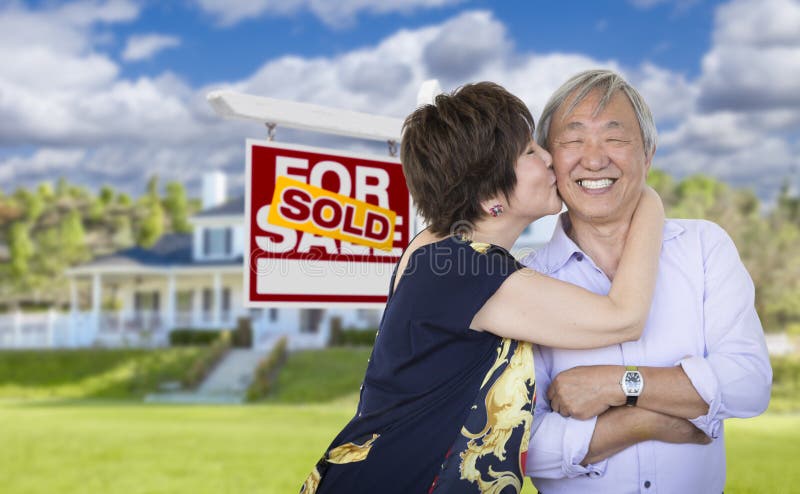 Attractive Affectionate Senior Chinese Couple In Front of Beautiful House and Sold For Sale Real Estate Sign. Attractive Affectionate Senior Chinese Couple In Front of Beautiful House and Sold For Sale Real Estate Sign.