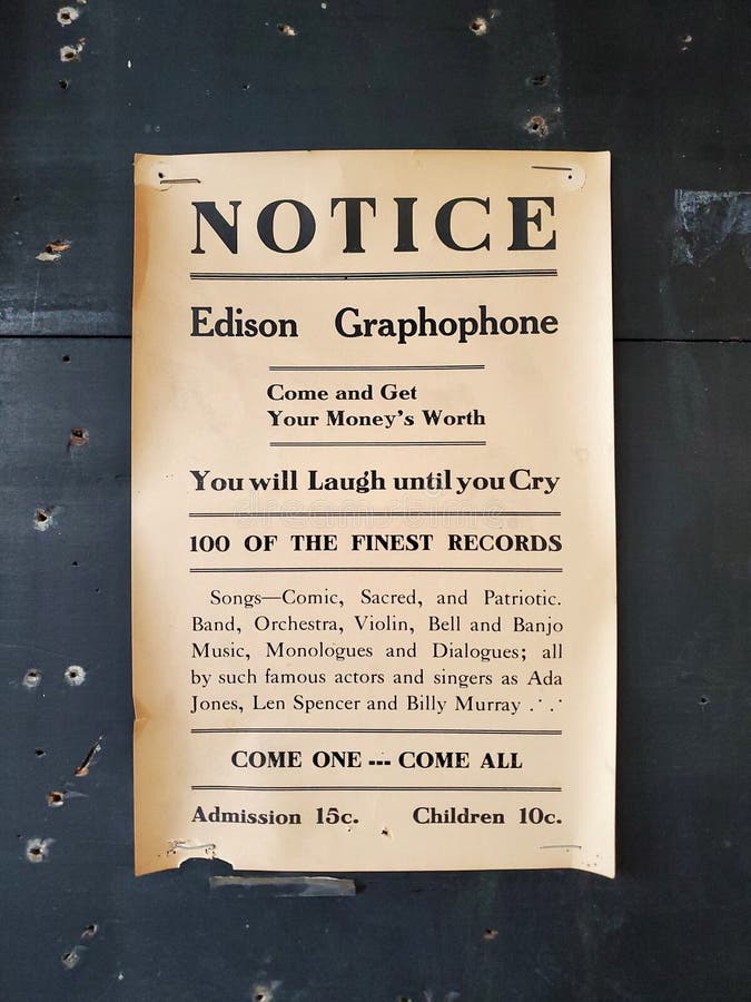 Affiche jaunâtre à l'ancienne faisant la publicité du graphophone edison agrippé à un mur noir. Message vintage rectangulaire imprimé sur papier moderne est un avis posté pour les chansons venir tout avec le prix d'admission de quinze cents et le coût inférieur pour les enfants assidus. cent des meilleurs disques annoncés.