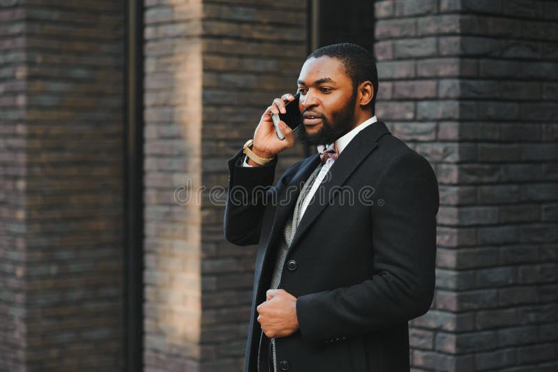 Affärskommunikation. lycklig ung afrikan-man på formella kläder som pratar på mobiltelefon och leende medan han står utomhus royaltyfri foto
