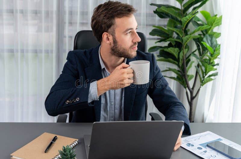 Affärsman som arbetar med sin bärbara dator och dricker kaffe vid sitt skrivbord. enhet arkivbilder