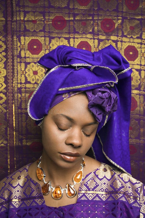 Portrait of an African American woman wearing traditional African clothing and closing her eyes in front of a patterned wall. Vertical format. Portrait of an African American woman wearing traditional African clothing and closing her eyes in front of a patterned wall. Vertical format.