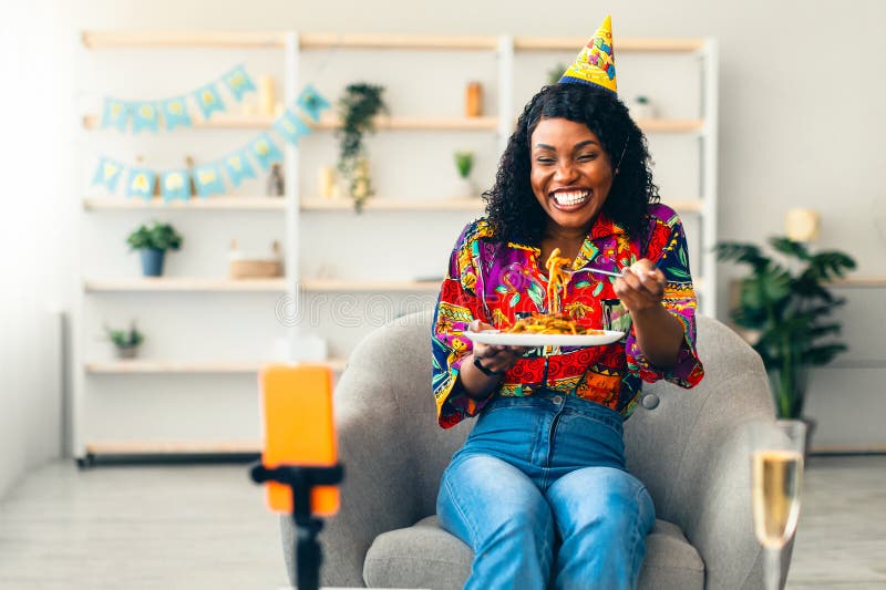 Africa: una donna mangia vicino allo smartphone durante una festa di compleanno online all'interno fotografie stock libere da diritti