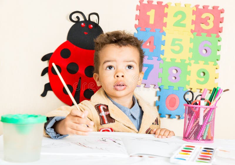 African American black boy drawing with colorful pencils in preschool at table