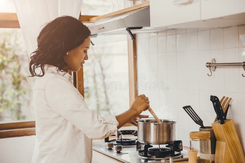 African American Black woman cooking boiling soup in the kitchen at home