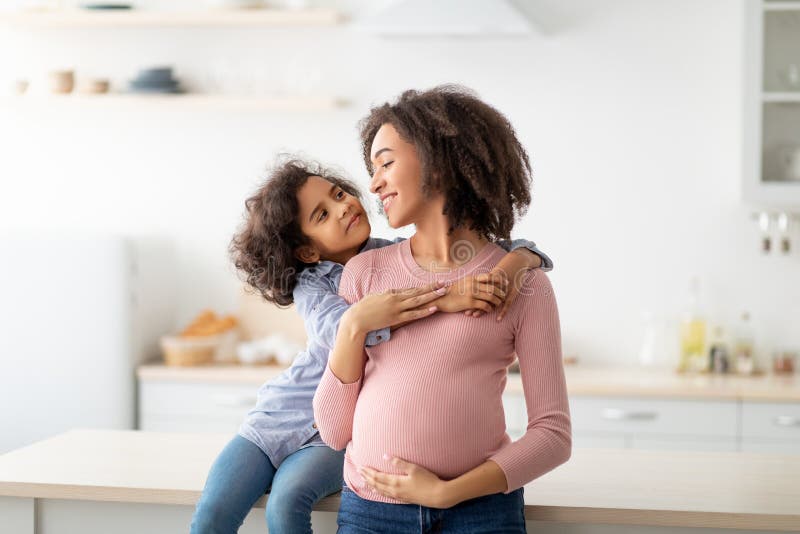 African American daughter hugging her pregnant mum from the back