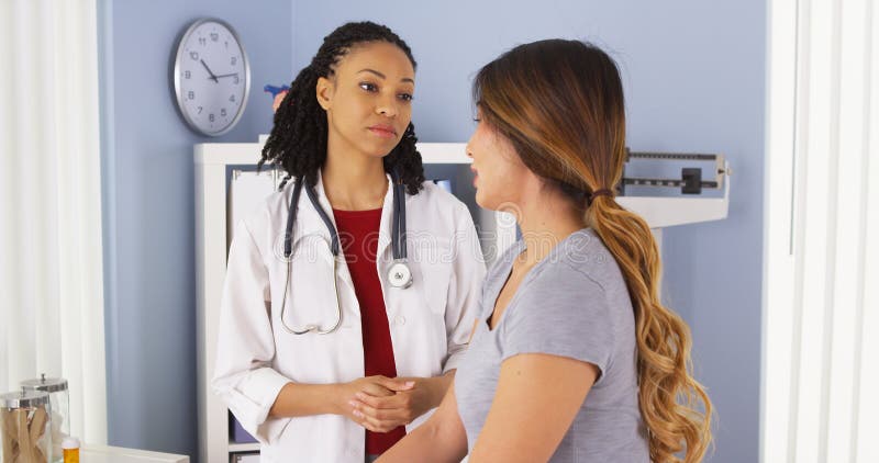 African American doctor talking to female Asian patient in exam room