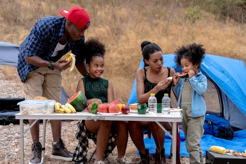 Happy black family with girl in forest. African american family  eating food during picnic