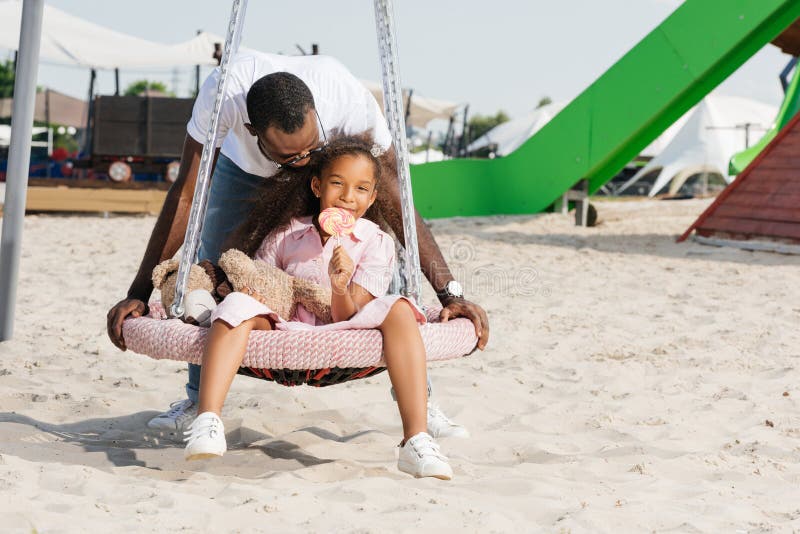 african american father pushing happy daughter with lollipop on spider web nest swing royalty free stock photos african american father pushing happy daughter with lollipop on spider web nest swing royalty free stock photos
