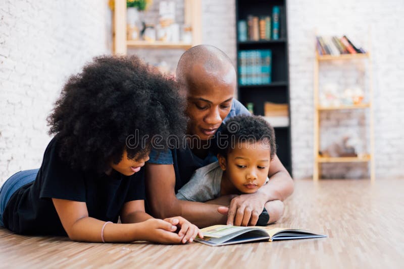 African American father reading a fairy tale fable story for kids at home. Happy family lying on the floor indoors