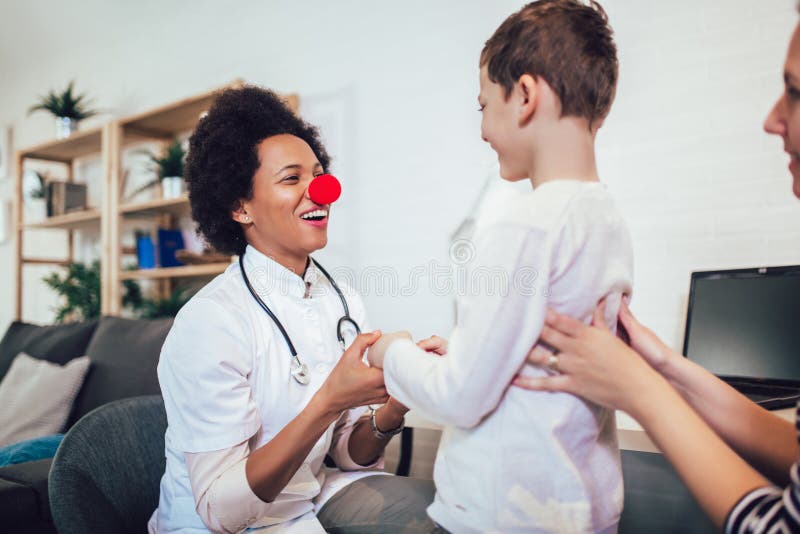 African American female pediatrician with stethoscope and clown nose talking to boy
