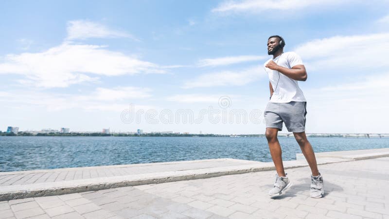 African American Guy in Headphones Jogging Along River in City Stock ...